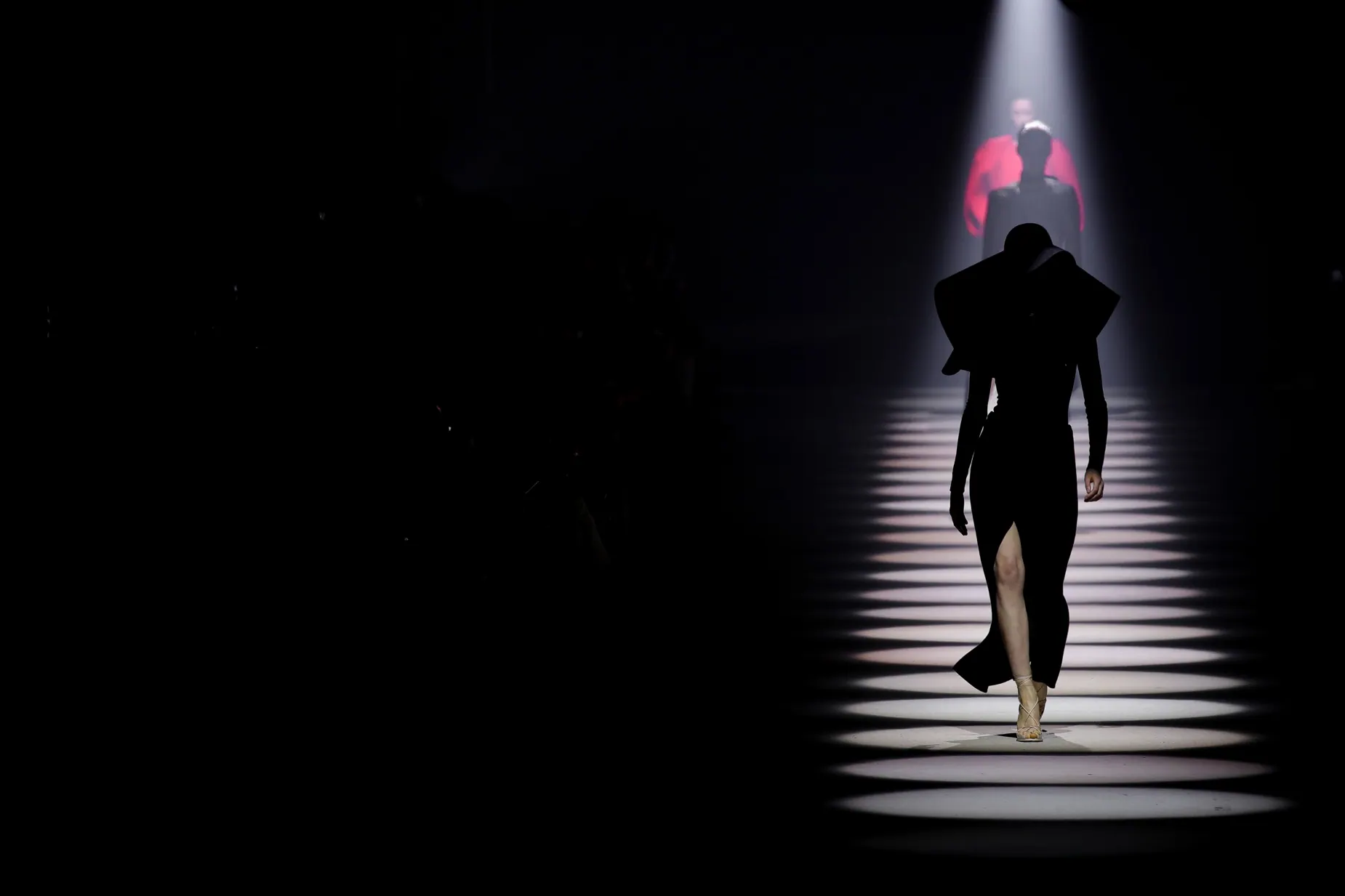 A Givenchy runway model approaches through a dark, spotlit runway