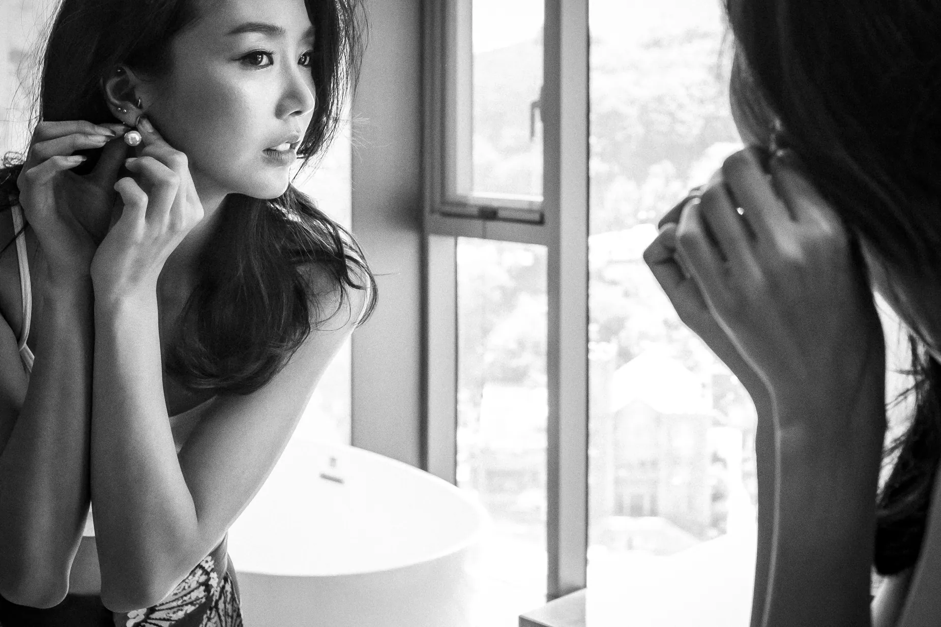 Black and white portrait of woman adjusting an earring by a mirror